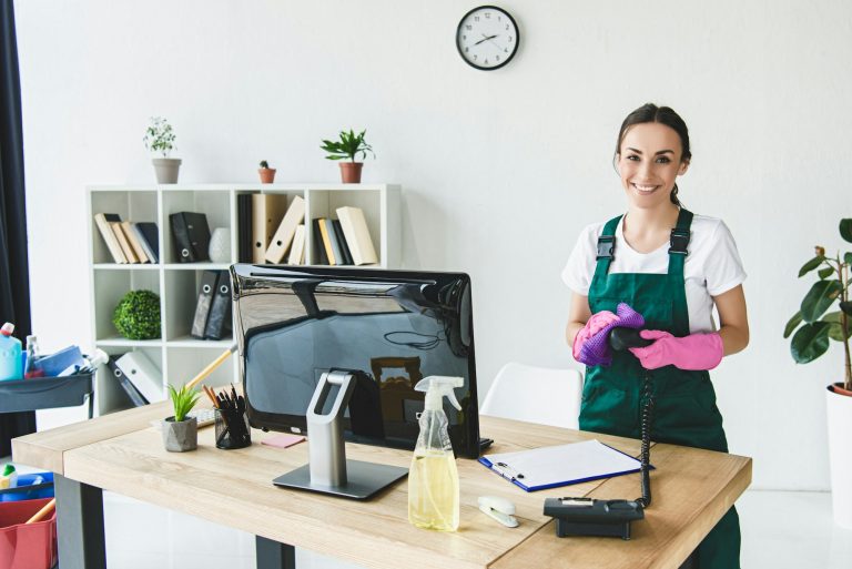beautiful young professional cleaner smiling at camera while cleaning modern office